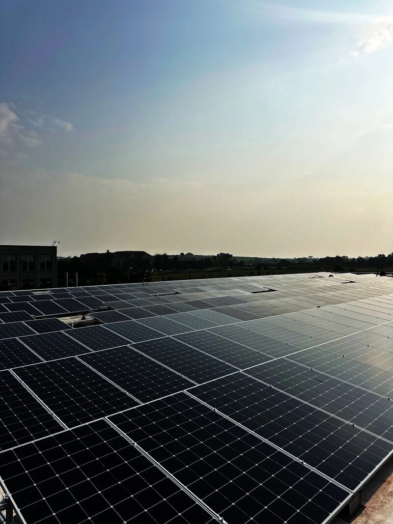A large rooftop array of dark solar panels stretching into the distance under a hazy sky
