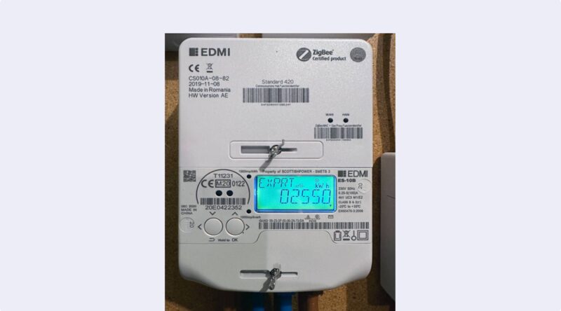 A close-up of an EDMI smart electricity meter with a blue display showing an export reading, mounted on a wall