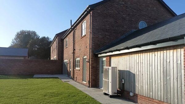 An air source heat pump unit installed outside a modern brick and timber-clad house with a lawn