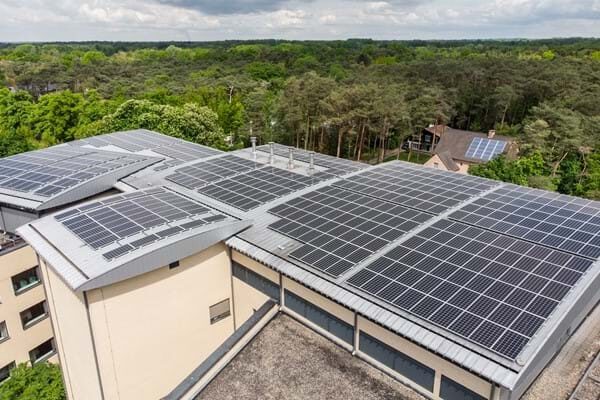 A large rooftop array of solar panels mounted on a standing seam metal roof of a building surrounded by trees