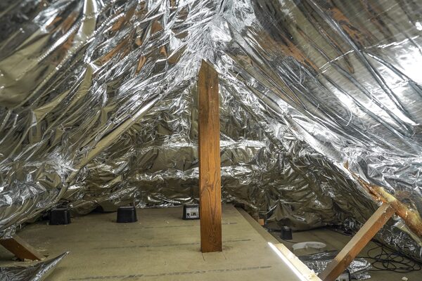 A loft space lined with reflective foil insulation draped over the rafters, with a wooden support post and boarded floor
