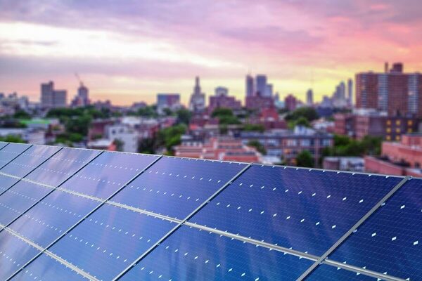 Rooftop solar panels with a city skyline at sunset in the background