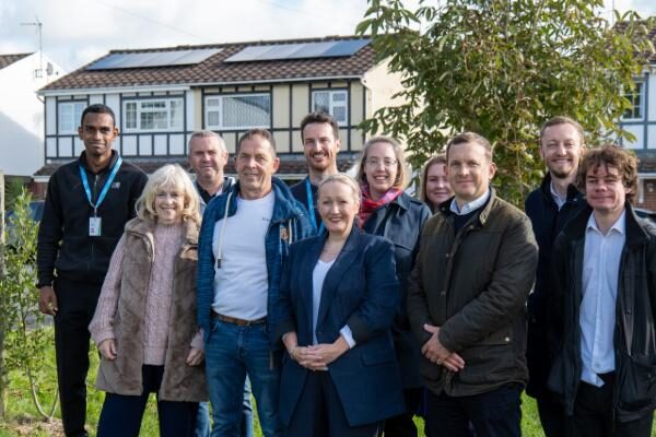 A group of people standing outside a house with rooftop solar panels
