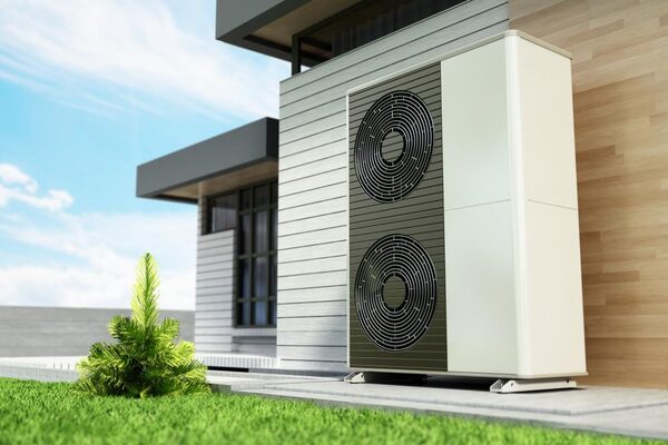 A large air source heat pump unit installed outside a modern house on a paved base beside a lawn