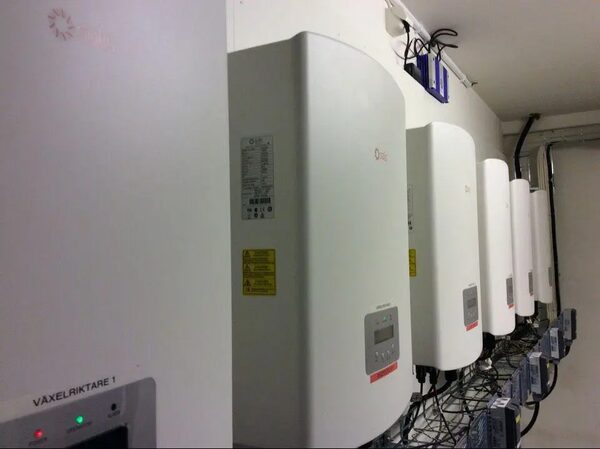 A row of white Solis solar inverters mounted on a wall in an electrical room, wired to grid connection equipment