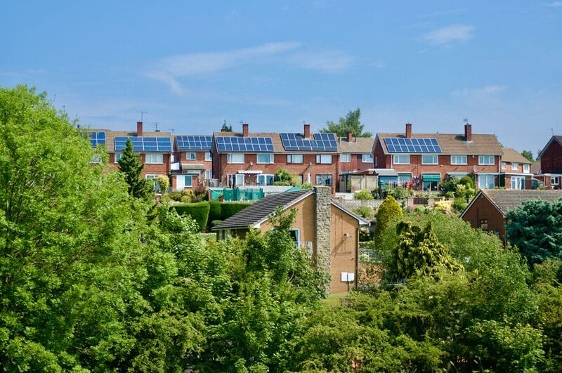 A row of brick houses with rooftop solar panels seen above trees on a sunny day