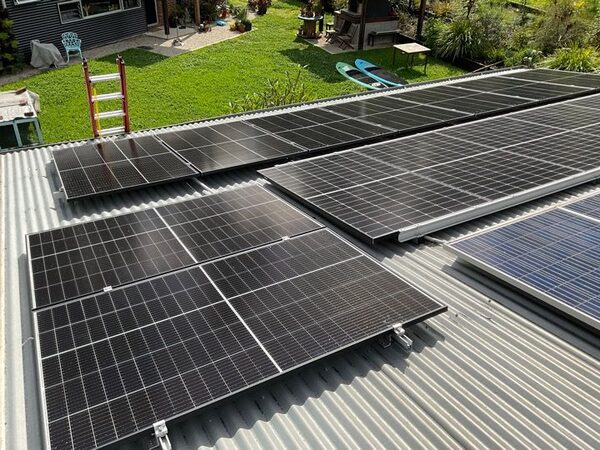 Solar panels being installed on a corrugated metal roof of a house with a garden in the background