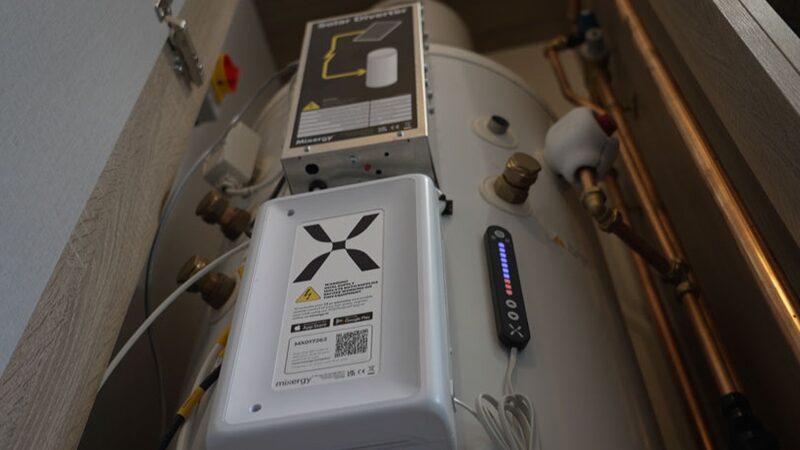 A Mixergy hot water cylinder with its Solar Diverter control unit installed in a cupboard with copper pipework
