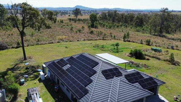 Aerial view of a rural house with dark solar panels covering its tiled roof, surrounded by open countryside