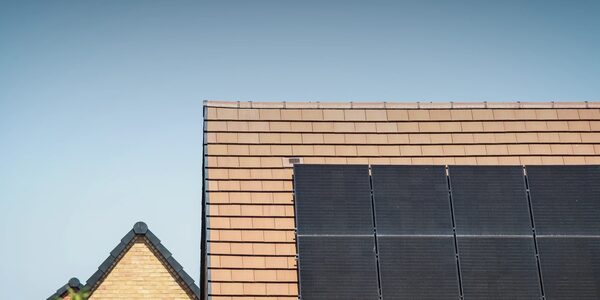 Solar panels mounted on the tiled roof of a house against a clear blue sky