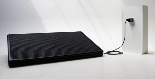 A black plug-in solar panel connected by cable to a small white wall-mounted unit, shown in a studio setting