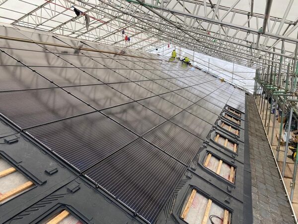 Workers on scaffolding installing a large array of solar panels on a roof with in-roof mounting frames