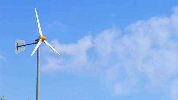 A small domestic wind turbine with three white blades and a tail fin mounted on a pole against a blue sky