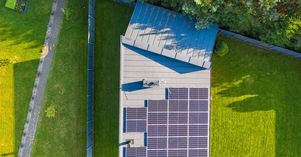 Aerial view of a house roof with solar panels installed, surrounded by a green garden
