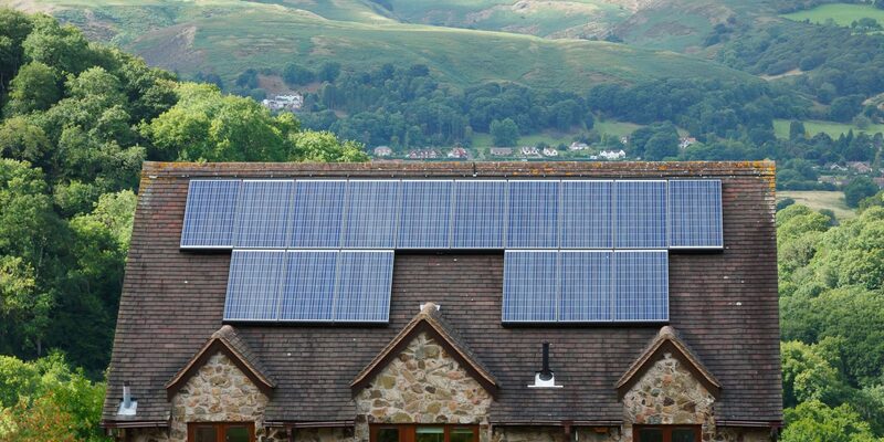 A stone farmhouse with solar panels on its roof, set behind a dry stone wall in the countryside