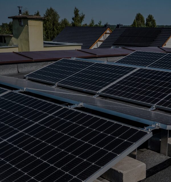 Rows of solar panels mounted on a flat residential rooftop with houses and trees in the background