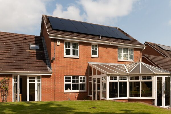 A brick UK house with solar panels on the roof and a conservatory