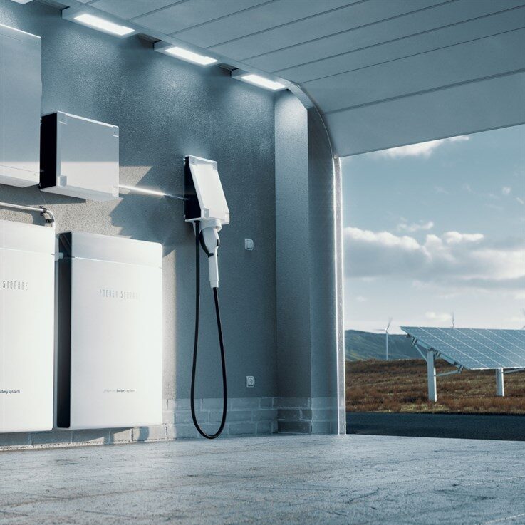 A garage wall with home battery storage units and an EV charge point, with solar panels and a wind turbine visible outside