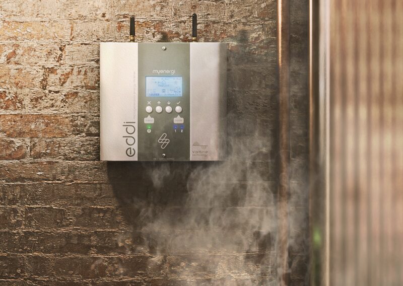 A myenergi eddi solar hot water diverter unit mounted on a brick wall with steam rising beside it