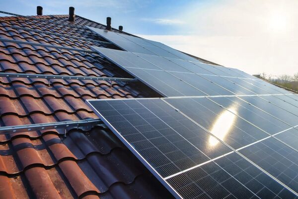 Solar panels being installed on a terracotta tiled roof with mounting rails visible