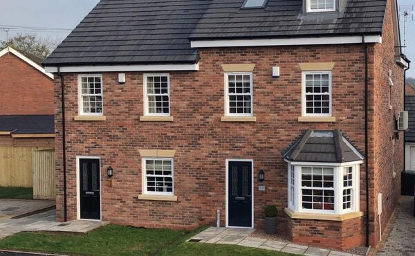 A new-build brick semi-detached house with an air source heat pump unit mounted on its side wall