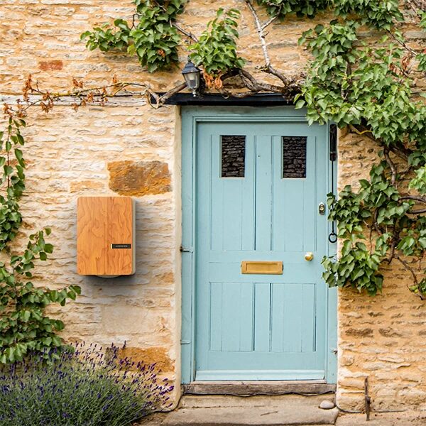 An Andersen A3 wooden-cased EV charger mounted on a stone cottage wall beside a pale blue front door