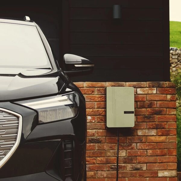 A beige Andersen EV home charge point mounted on a brick wall next to a parked black electric car