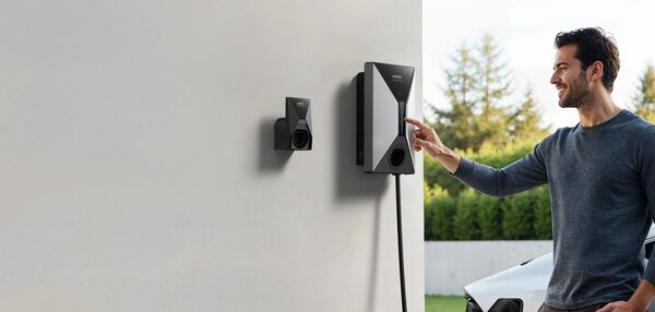 A man touching a wall-mounted Anker SOLIX EV charger with cable outside a house