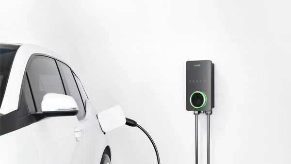 A white electric car plugged in with a cable connected to a black Autel wall-mounted EV charger on a white wall