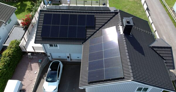 Aerial view of a house roof covered with solar panels, with a white car parked in the driveway below