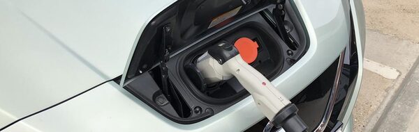 A charging cable plugged into the charge port of a pale green Nissan Leaf electric car