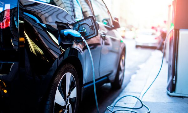 A black electric car plugged into a public charging point on a city street