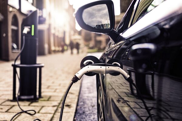 An electric car plugged in with a charging cable at a public kerbside EV charge point on a cobbled street