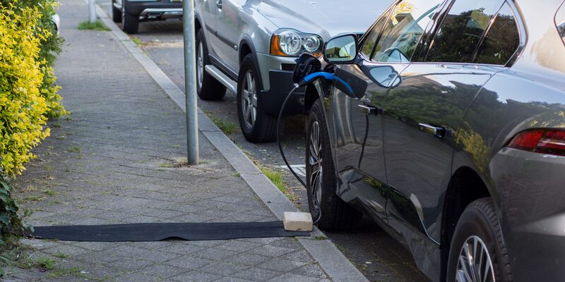 An electric car parked at the kerb charging via a cable run across the pavement from a house