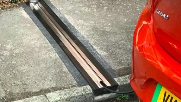A red electric car charging via a cable from a flush pavement-embedded kerbside charging unit