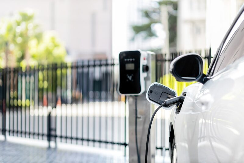 A white electric car plugged in and charging at a wall-mounted EV charge point outdoors