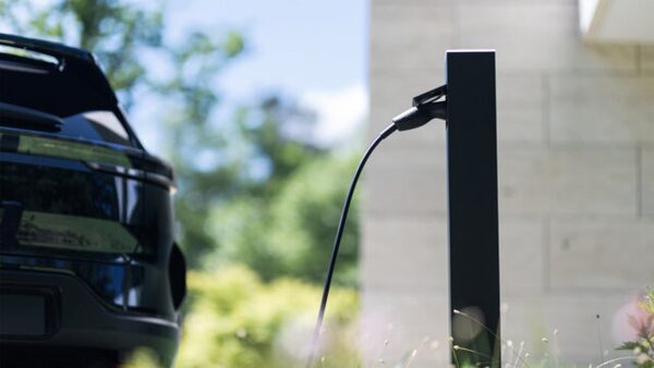 A black EV charging post outside a house with a charging cable plugged into a dark car