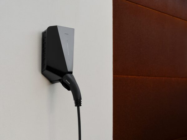 A black Easee wall-mounted EV charger with a tethered charging cable plugged in, mounted on a white wall