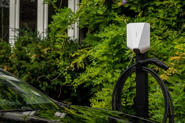 A white Easee electric car charge point mounted on a black post beside a car in a garden
