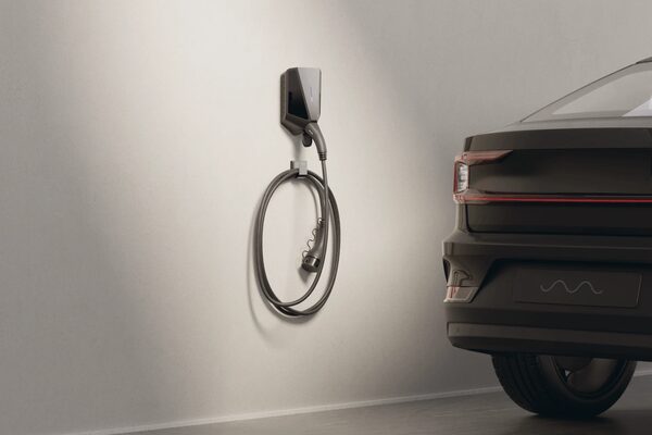 A black Easee wall-mounted EV charger with coiled cable next to a dark electric car