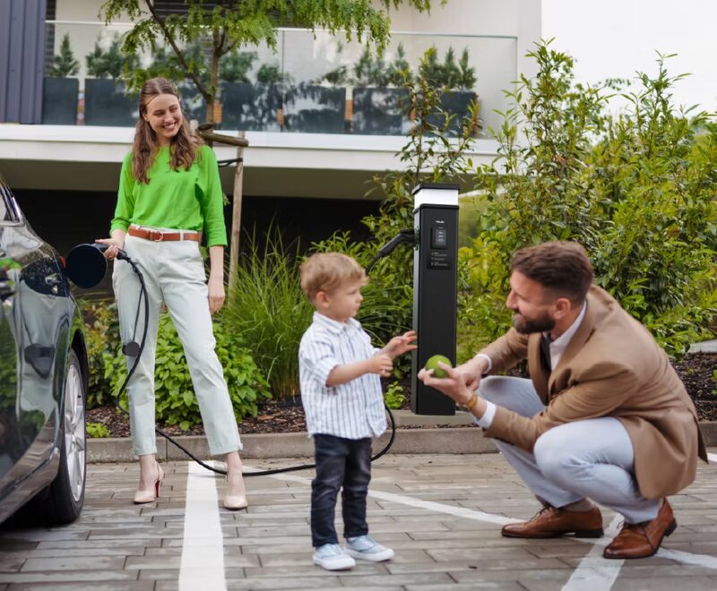 A family charging an electric car with a wall-mounted home EV charge point outside a modern house