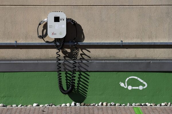 A wall-mounted electric vehicle charge point with coiled cables above a green wall painted with an electric car symbol