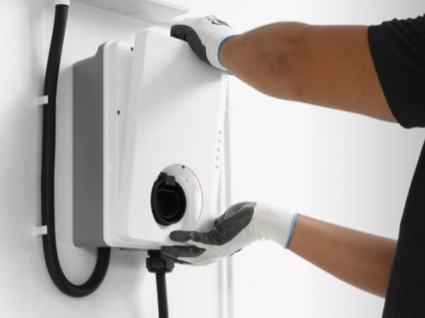A gloved installer fitting the front cover onto a wall-mounted white EV charge point