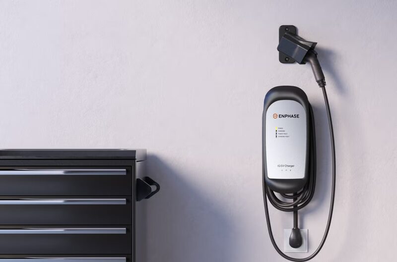 An Enphase IQ EV Charger wall-mounted in a garage next to a black tool chest, with charging cable holstered