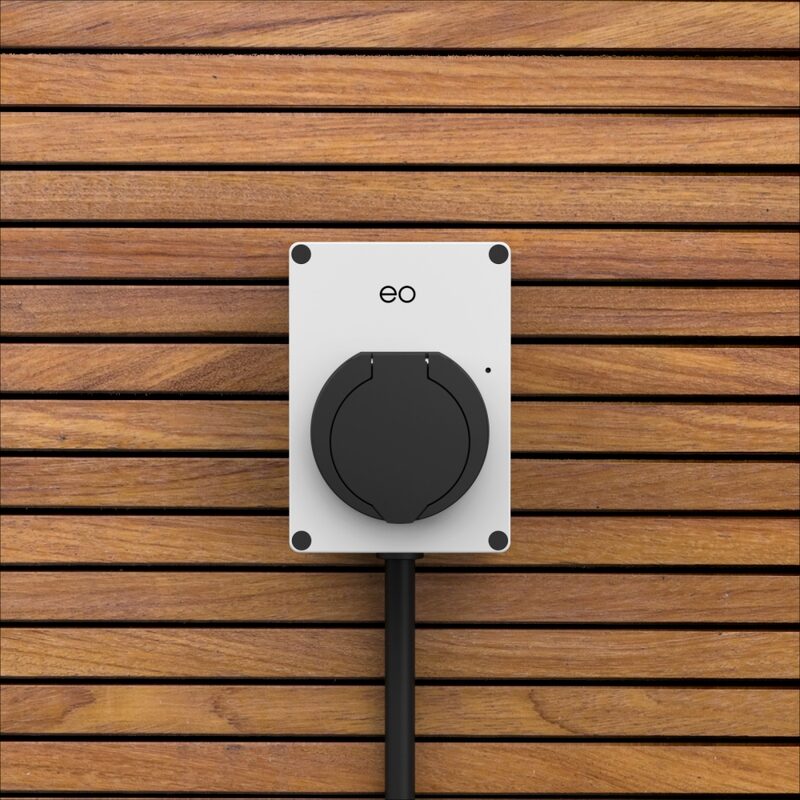 A white EO wall-mounted EV charging point with a black tethered cable on a wooden slatted wall