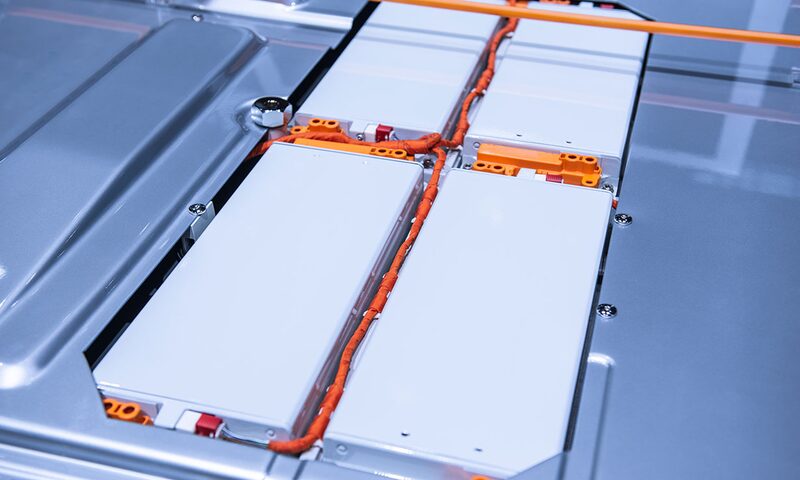 Close-up of an electric car battery pack with white modules and orange high-voltage cabling inside a metal casing