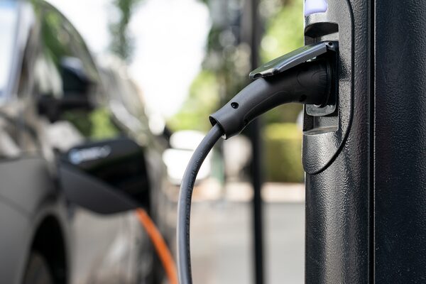 An electric car charging cable plugged into a public EV chargepoint, with the car blurred in the background