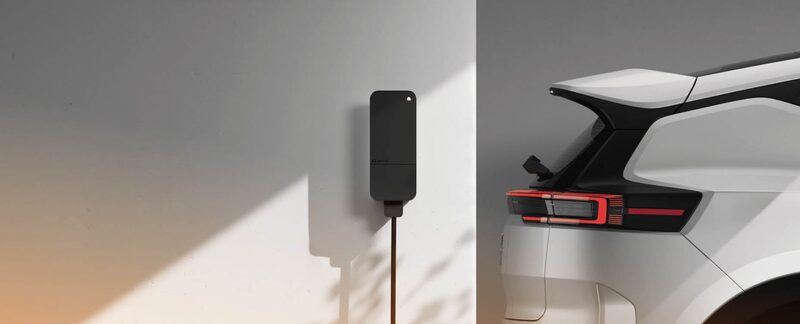 A wall-mounted black EV charger with cable next to the rear of a white electric car