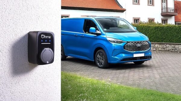 An Ohme EV charge point mounted on a wall next to a blue Ford electric van parked on a driveway