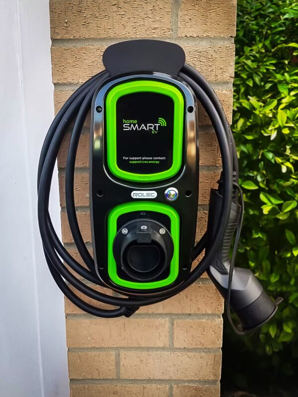 A Rolec Home Smart EV wall-mounted electric car charging point with coiled cable on a brick pillar outside a home